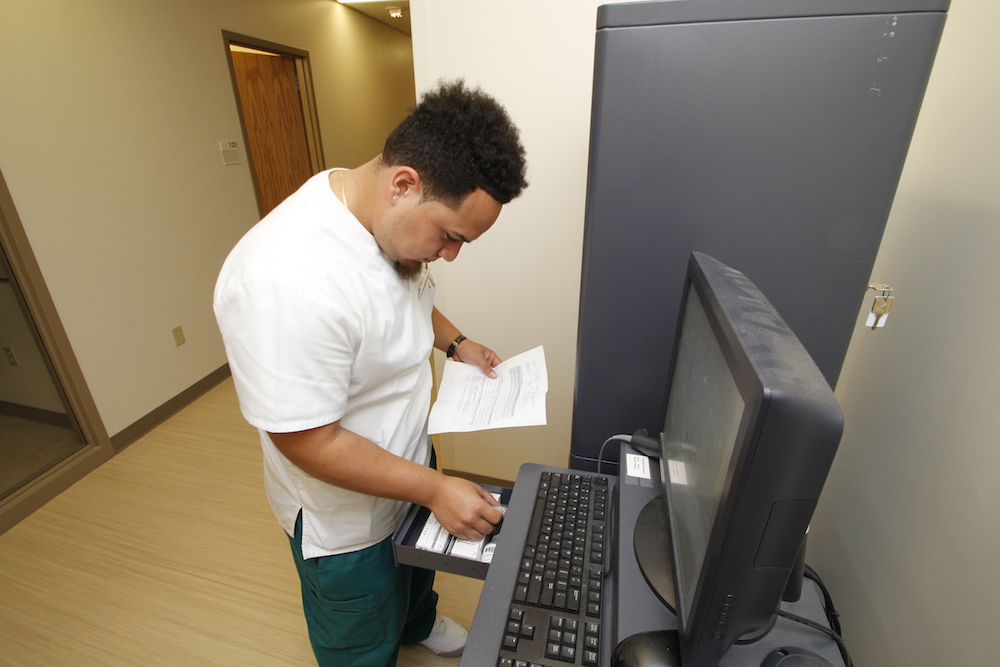 A male medical assistant student opens a drawer